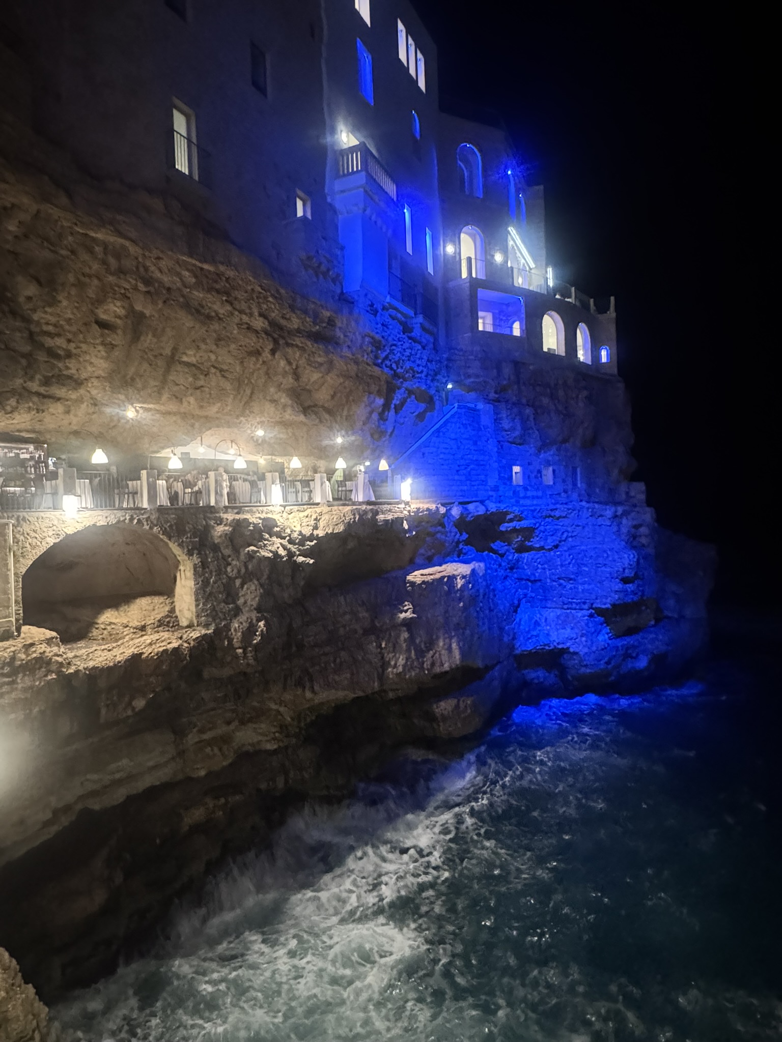 The blue-lit cliffside of Grotta Palazzese at night