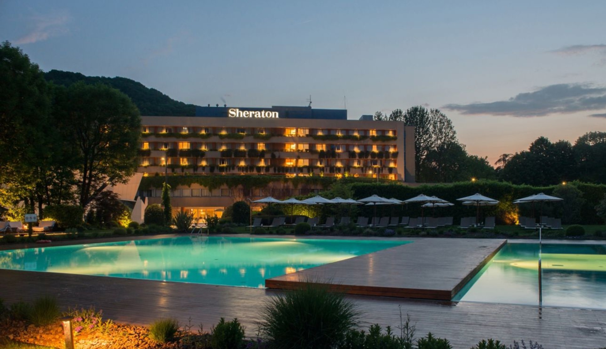 The Sheraton Lake Como Hotel lit up at dusk, seen across its outdoor pool